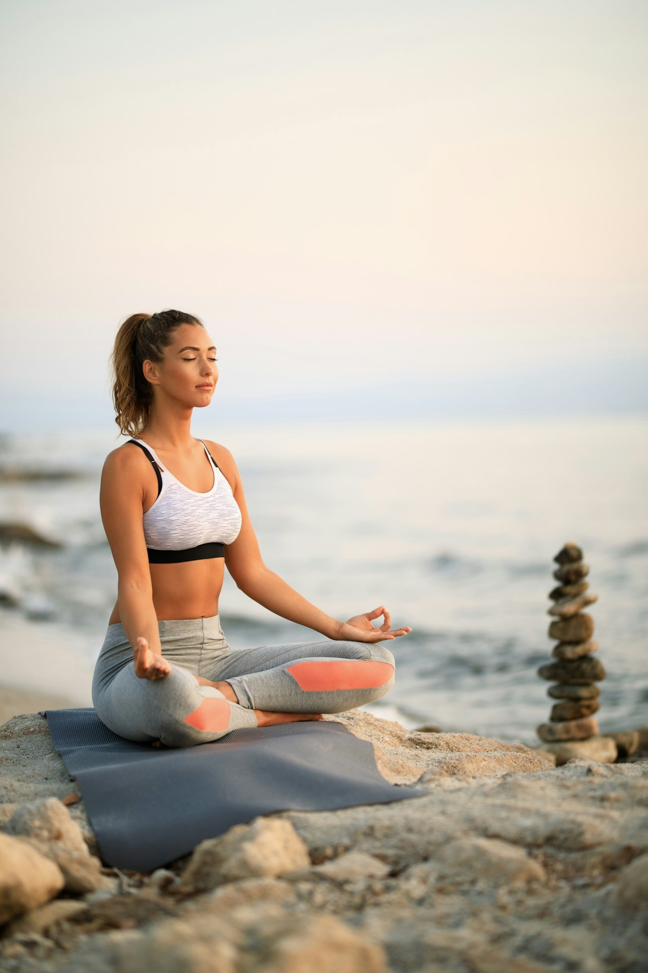 Zen-like woman meditating with eyes closed on a rock by the sea.